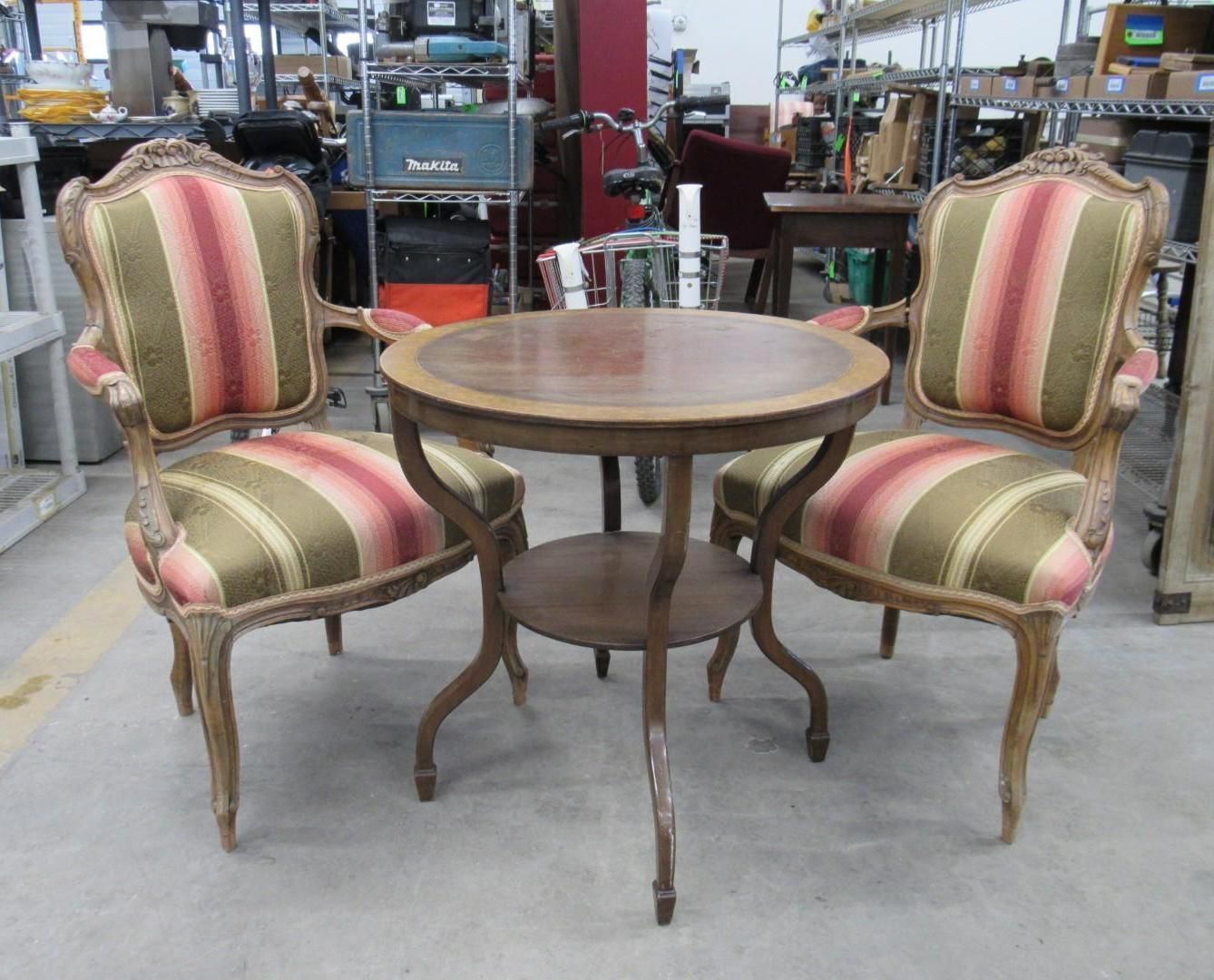 Two ornate armchairs with striped upholstery flank a small round table in a shop.
