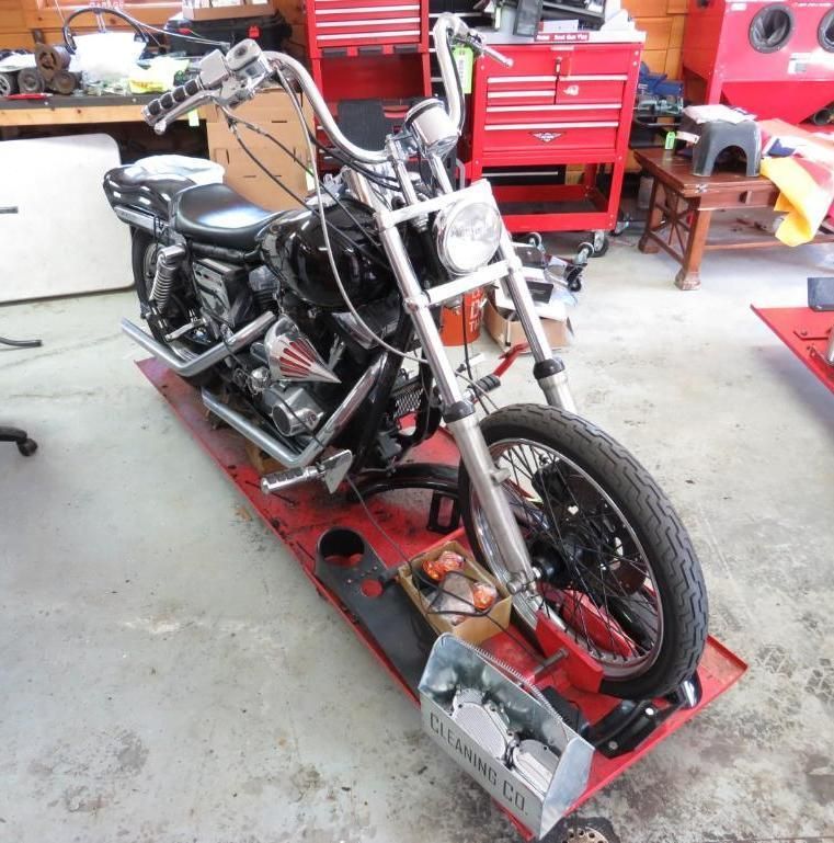 Black motorcycle on a red lift in a workshop, tools in background.