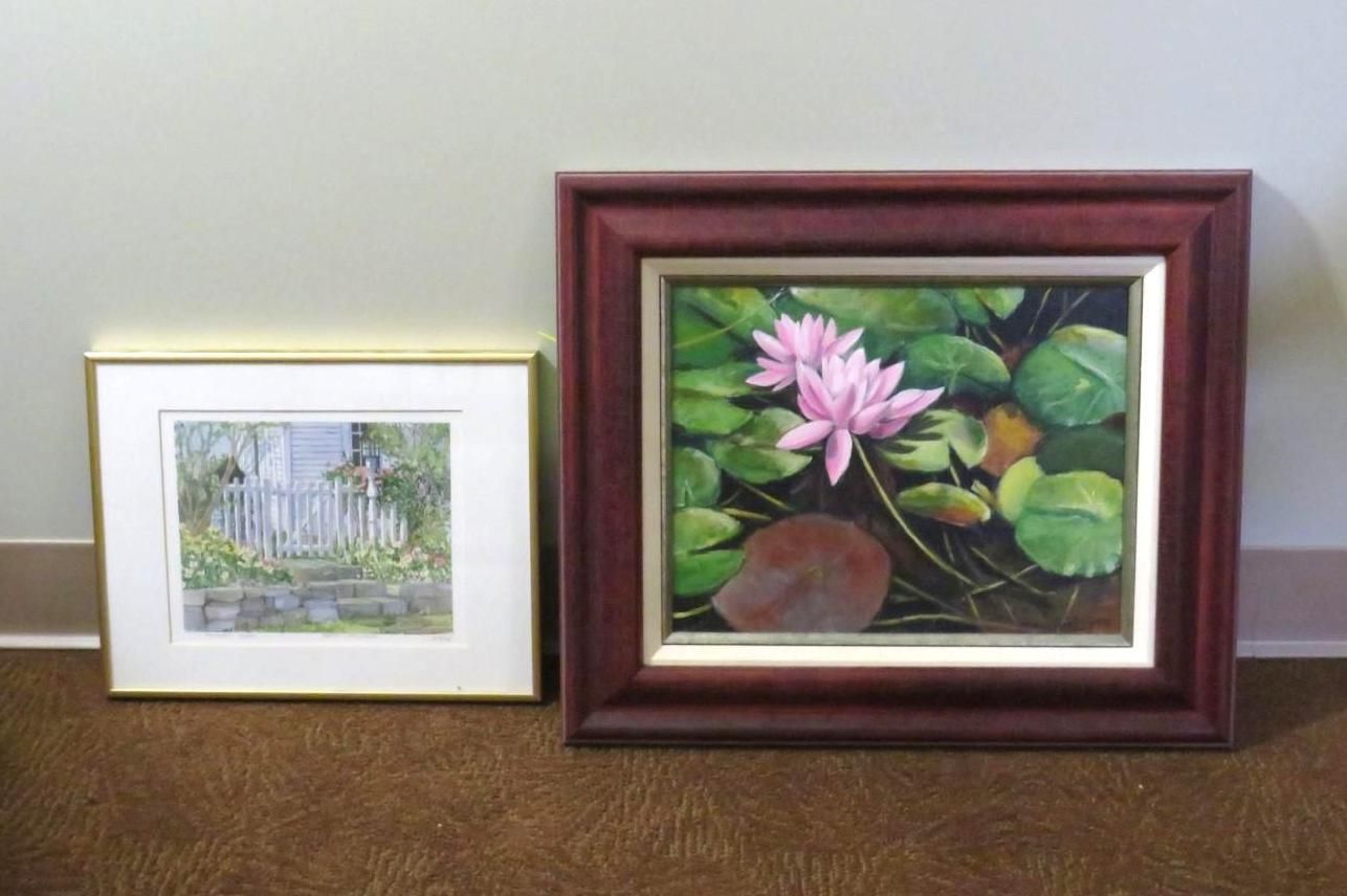 Two framed paintings: water lilies and a garden scene, displayed on a brown carpet against a beige wall.