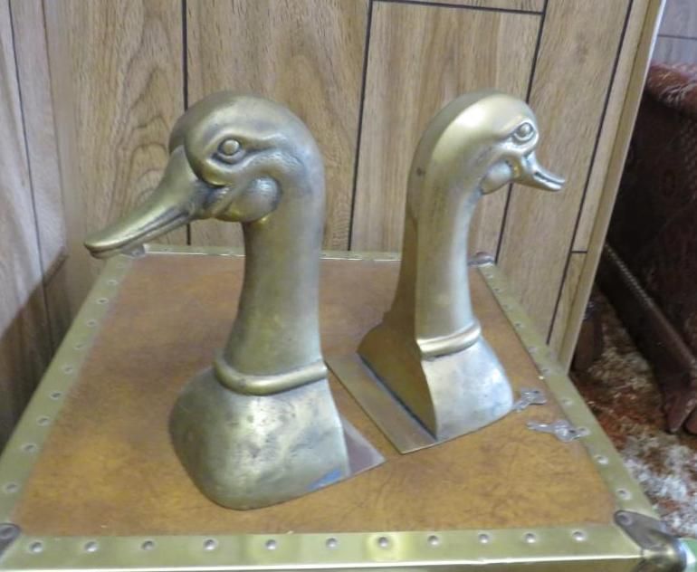 Two brass duck head bookends on a wood trunk.