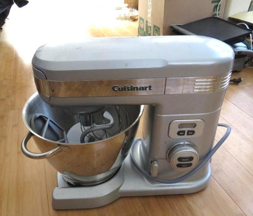 Silver Cuisinart stand mixer with stainless steel bowl and attachments, on a wooden floor.