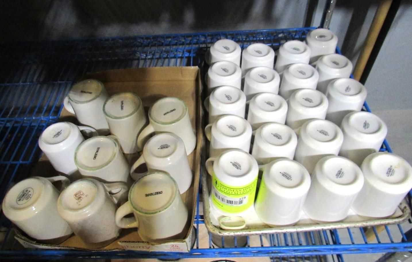 Mugs stacked on a blue wire shelf, some in a cardboard box, others on a tray, all upside down.