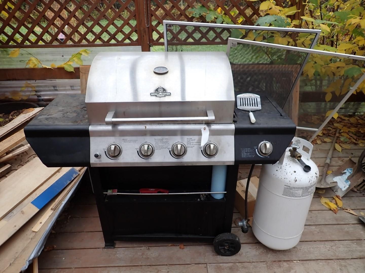 A black and silver gas grill with a propane tank, on a wooden deck.
