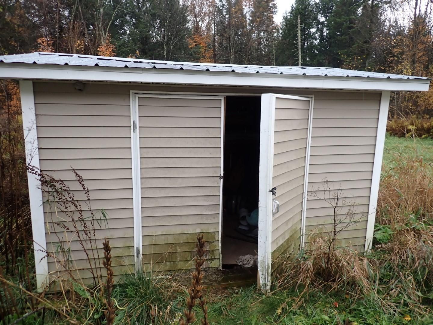 Beige shed with open doors in a grassy field.