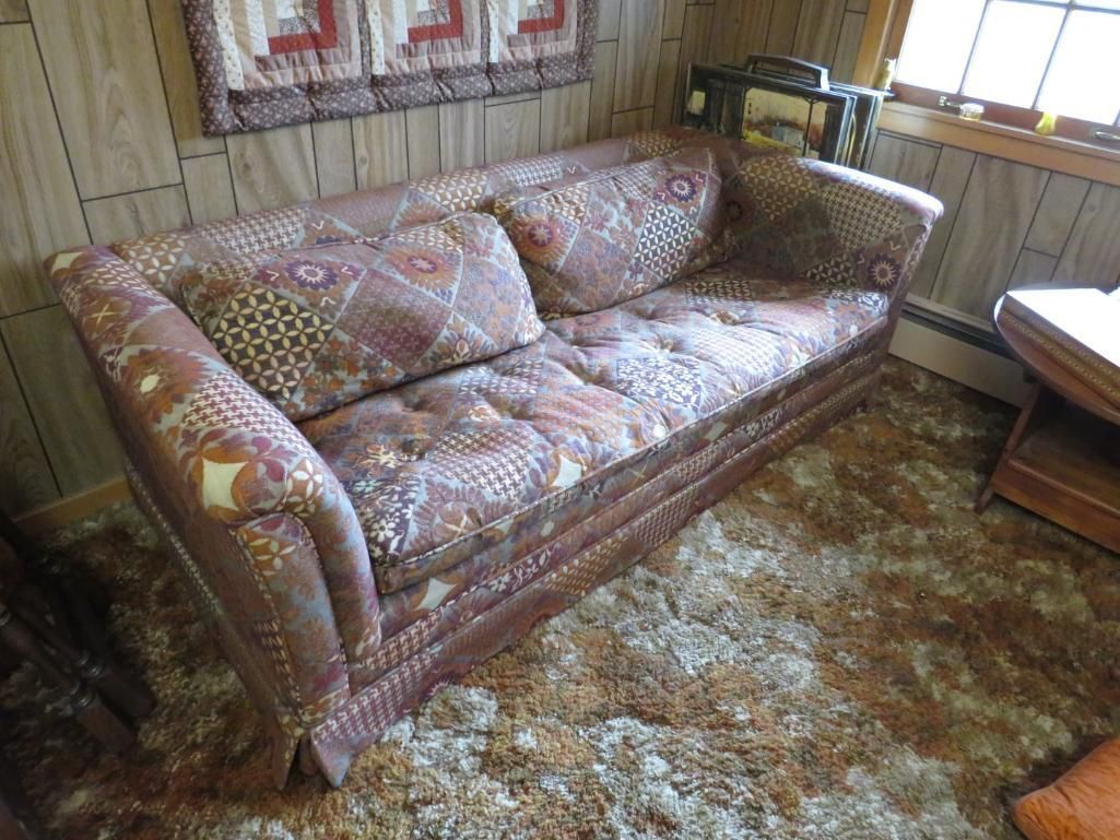Brown patterned sofa in a room with a patterned rug and wooden paneling.