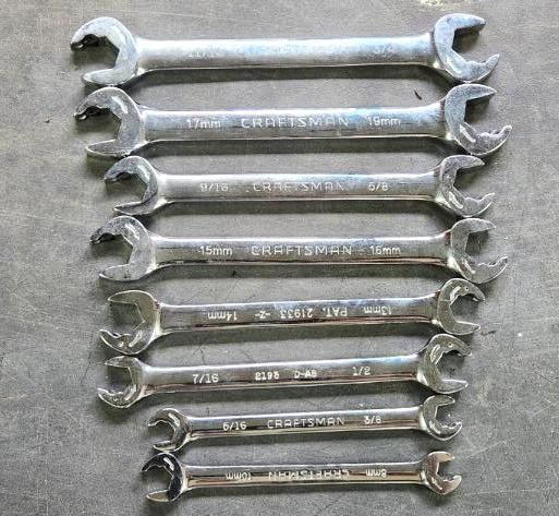 A collection of silver open-ended wrenches of various sizes arranged on a gray surface.