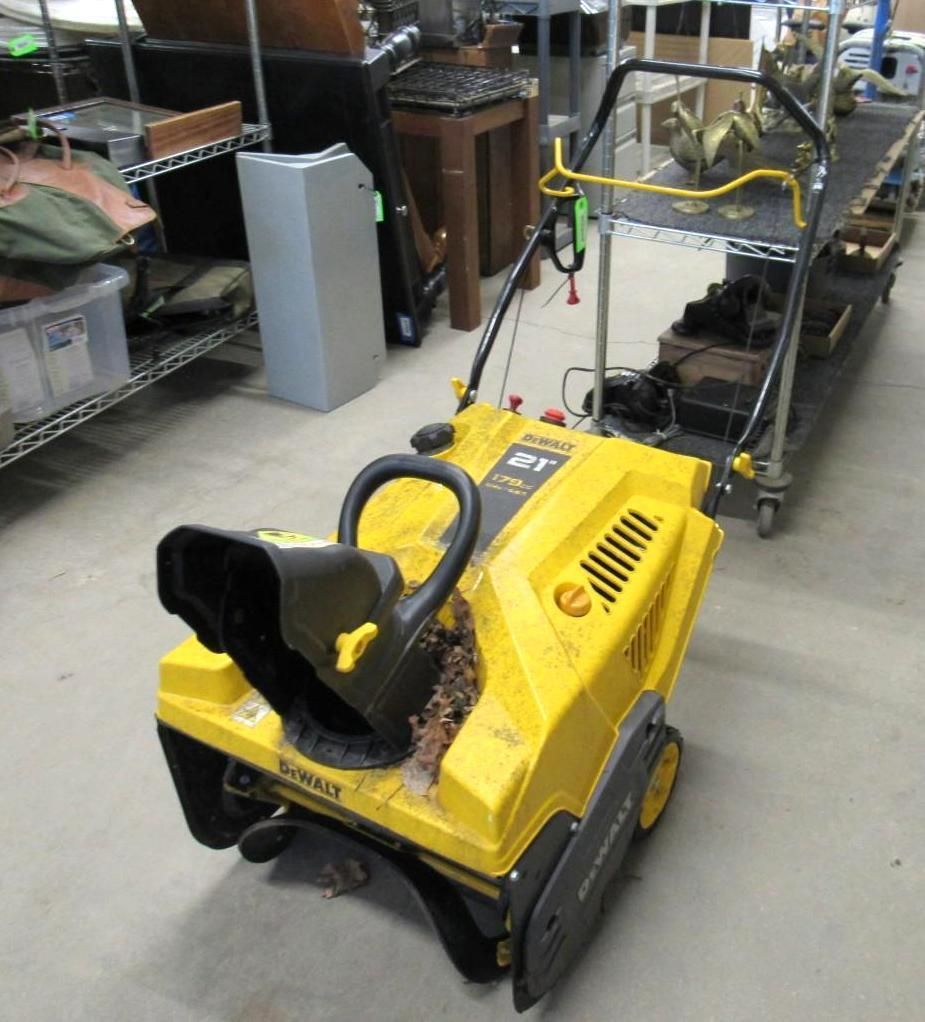 Yellow and black snow blower with a black chute in a storage area.