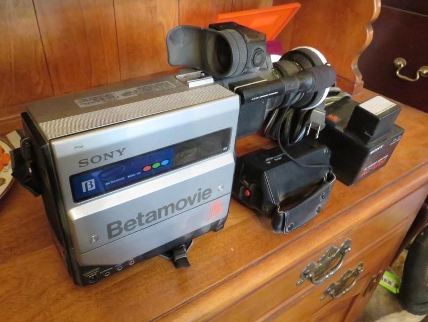 Sony Betamovie camera on a wooden dresser. Silver and black, with attached viewfinder and accessories.