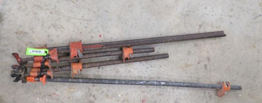 Several metal clamps lying on a concrete surface. They have orange and black components.