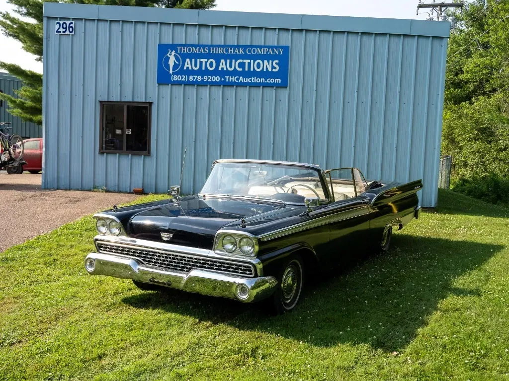 Black convertible car parked in front of an auto auction building on a grassy lawn.