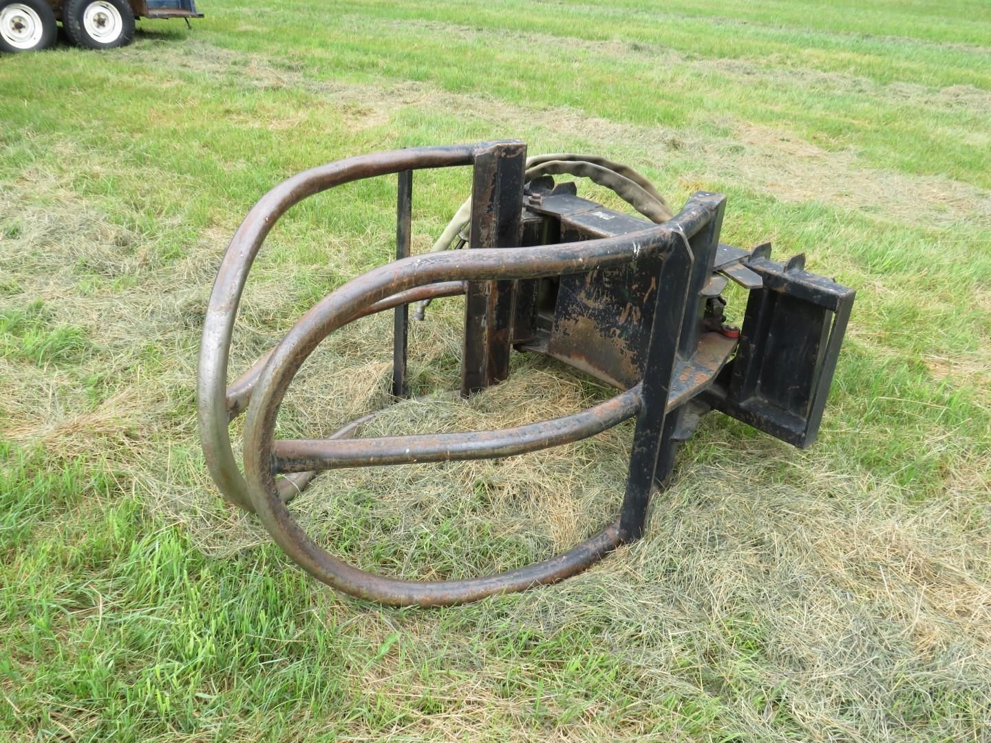 Black and steel-colored hay bale grabber on green grass, possibly for use on a farm.