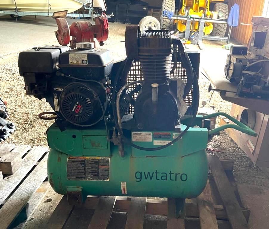 Green and black air compressor with a red engine on a wooden pallet in a workshop.