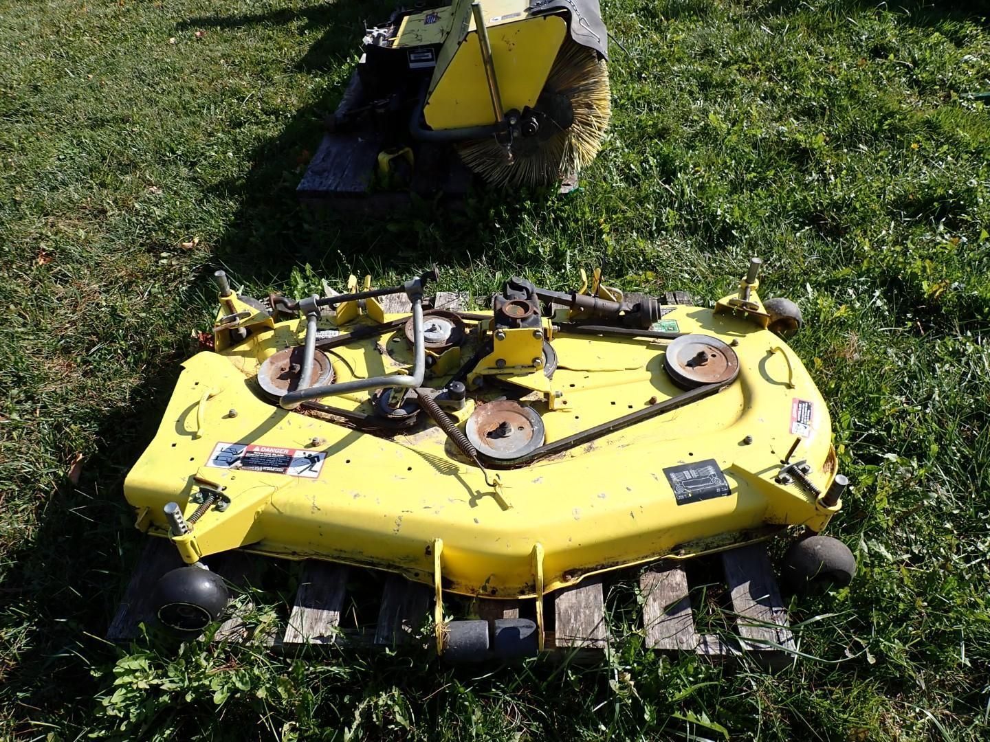 Yellow lawn mower tipped on its side in grass, with another mower behind it.