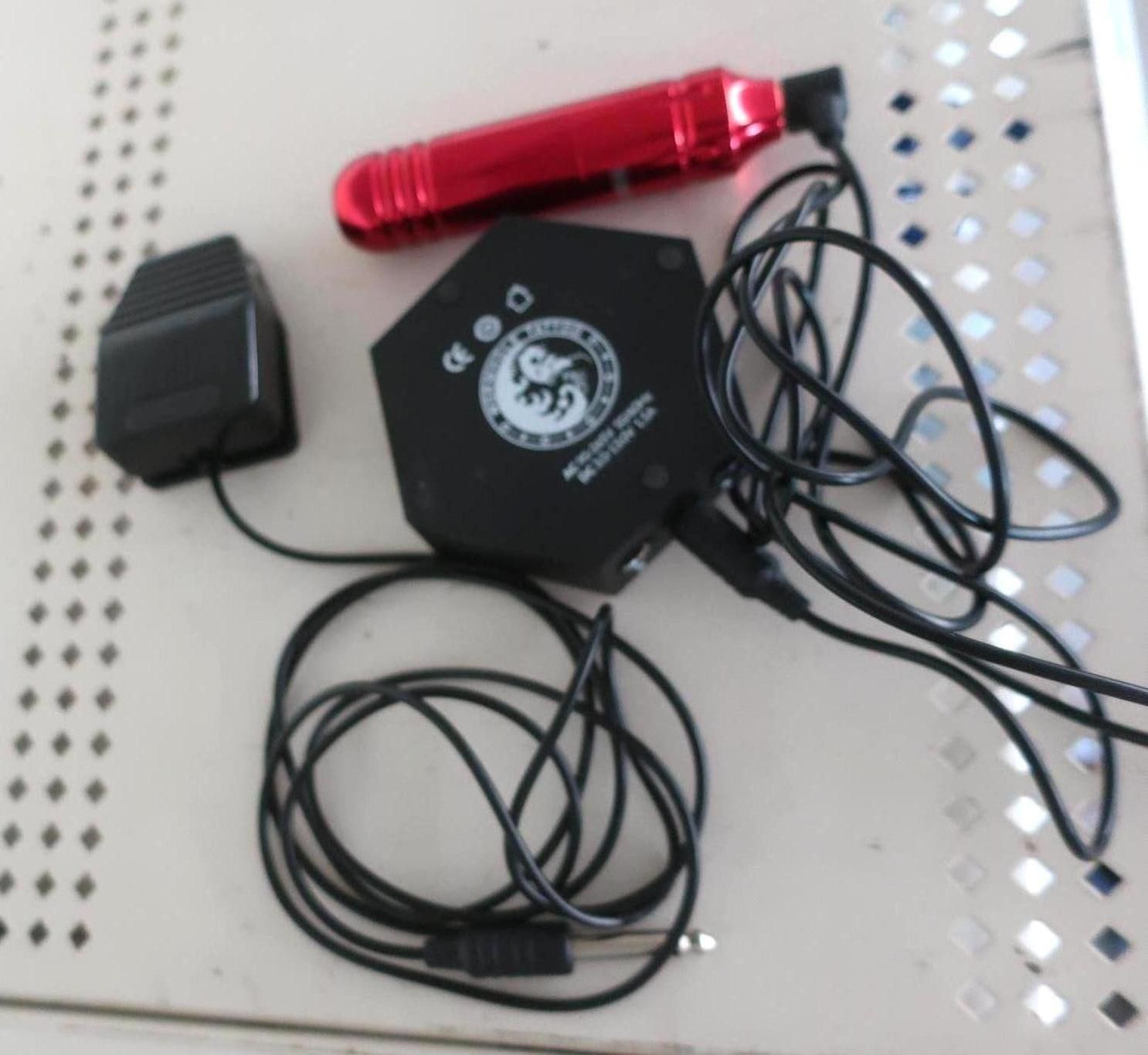 Tattoo equipment: red pen, black power supply with cords, and a black foot pedal on a surface.