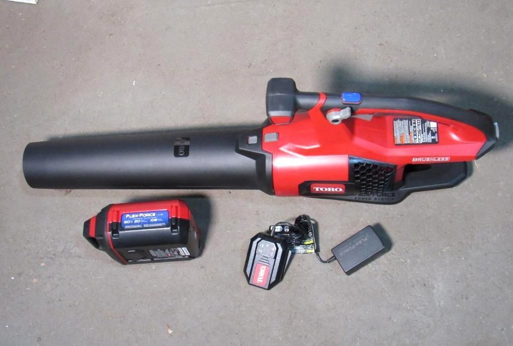 Red and black Toro leaf blower with a battery and charger on a floor.