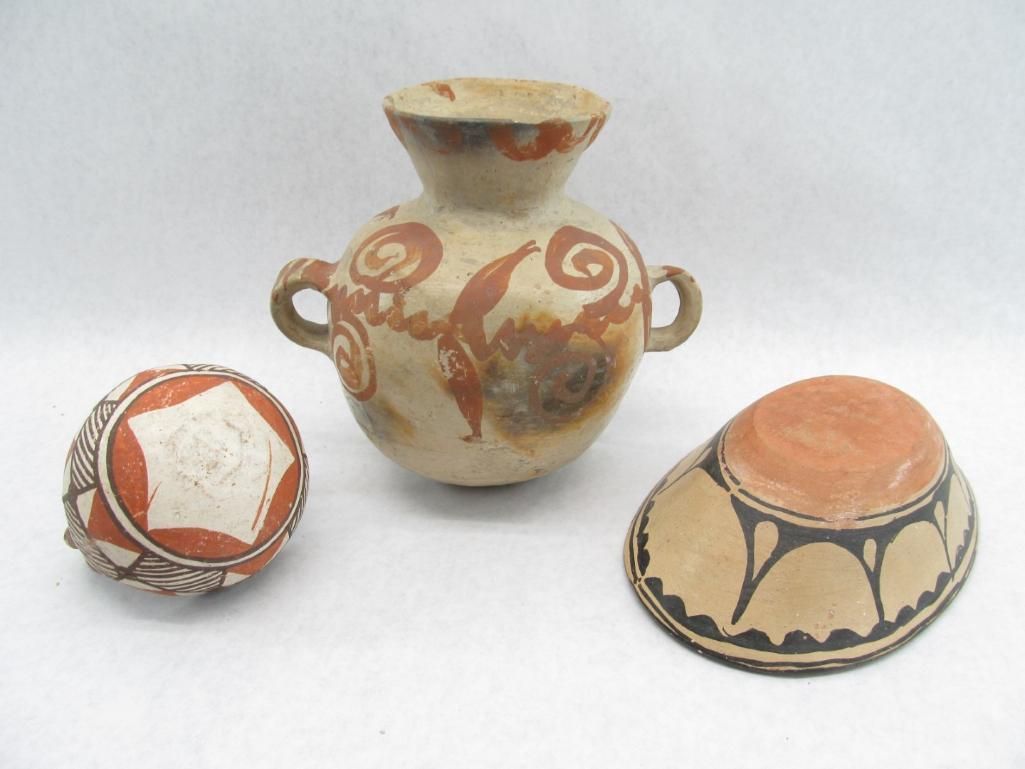 Three ancient pottery pieces: a vase with handles, a decorated bowl, and a round object.