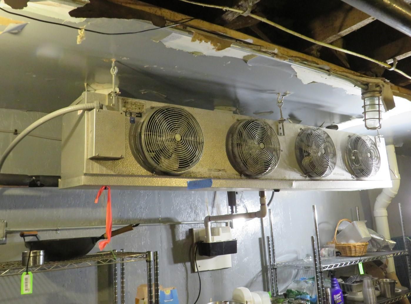 Overhead industrial refrigeration unit with four fans in a kitchen area.