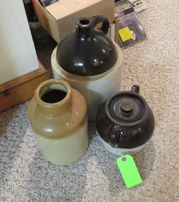 Three antique stoneware jugs of different sizes and colors on a carpeted floor.