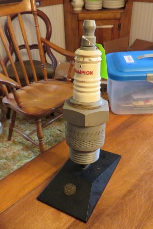 Large Champion spark plug sculpture on a black base, sitting on a wooden table.