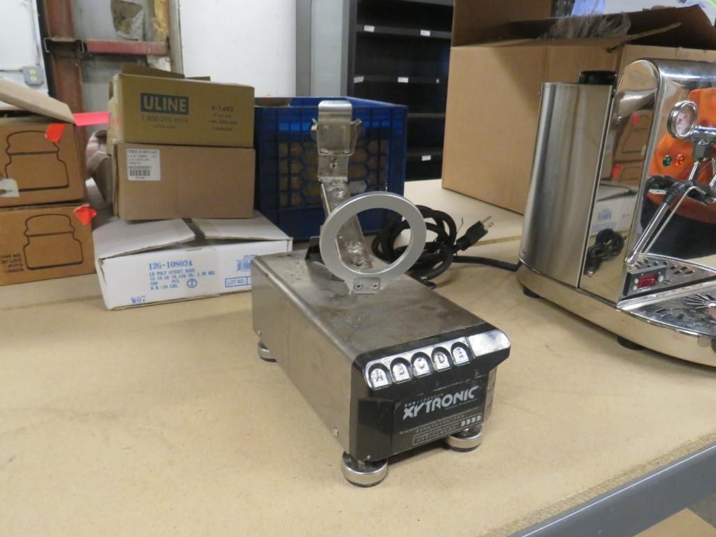Silver and black kitchen appliance with a handle, next to a silver espresso machine and boxes.