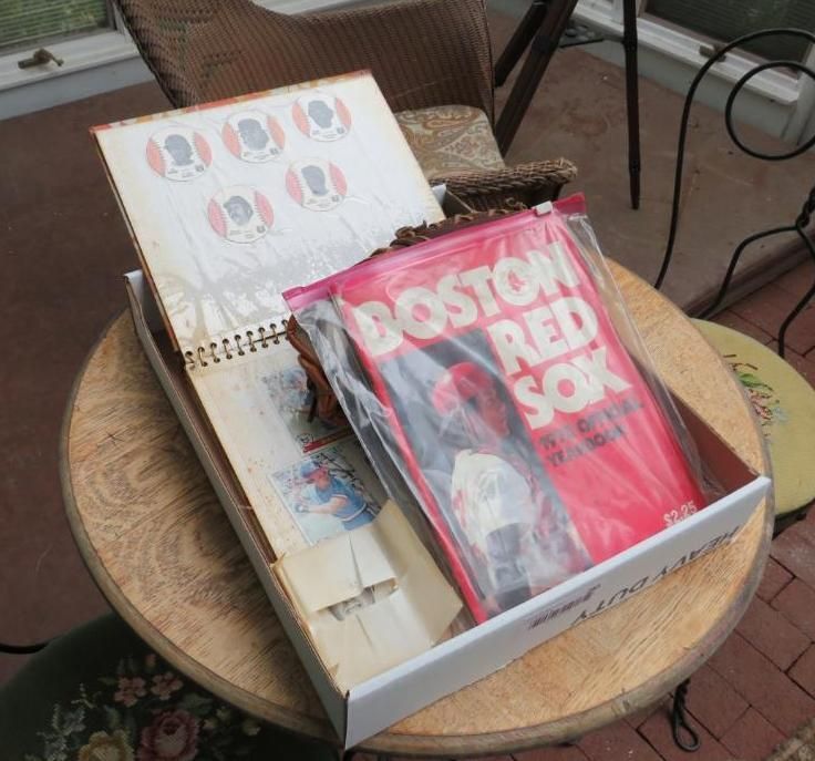 A box with a Boston Red Sox book and a stamp album on a table.