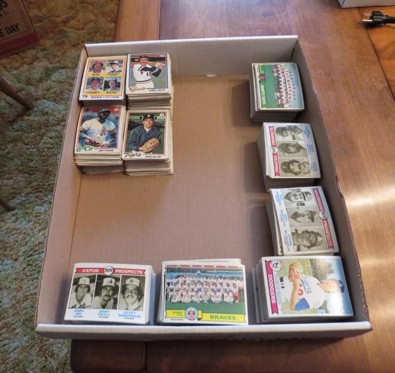 A cardboard box with stacks of vintage baseball cards, on a brown table.