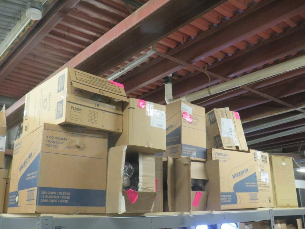 Cardboard boxes stacked on a shelf in a warehouse, with pink labels. Brown ceiling beams overhead.