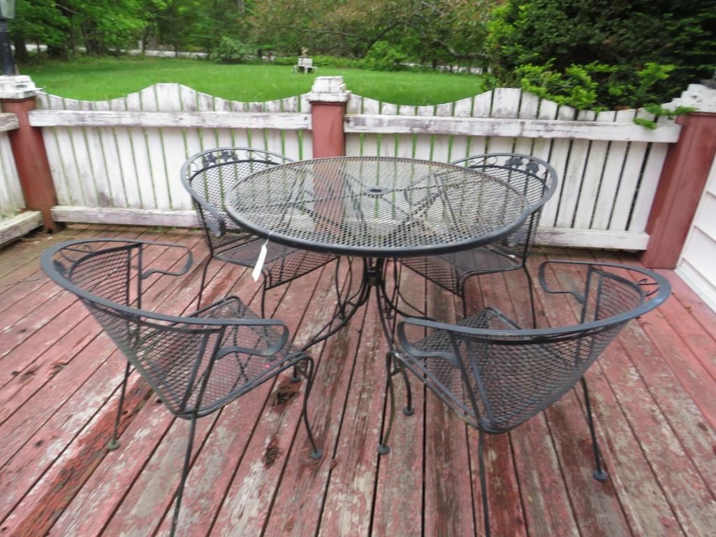 Outdoor patio set: round glass table, four black metal chairs.