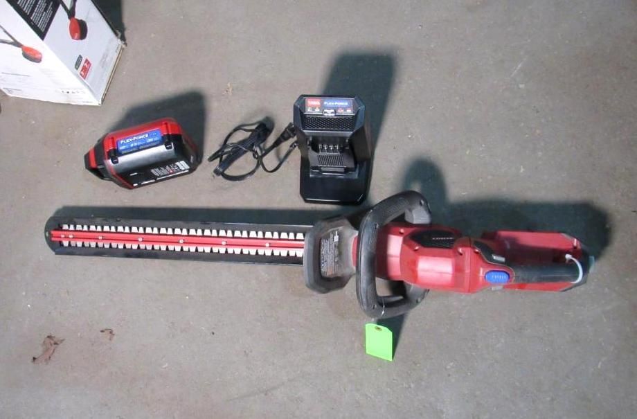 Red and black cordless Toro hedge trimmer with battery, charger, and box on gray concrete.