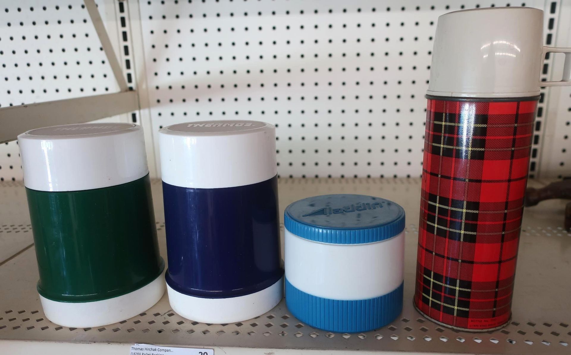 Four vintage thermos bottles of various colors on a shelf.