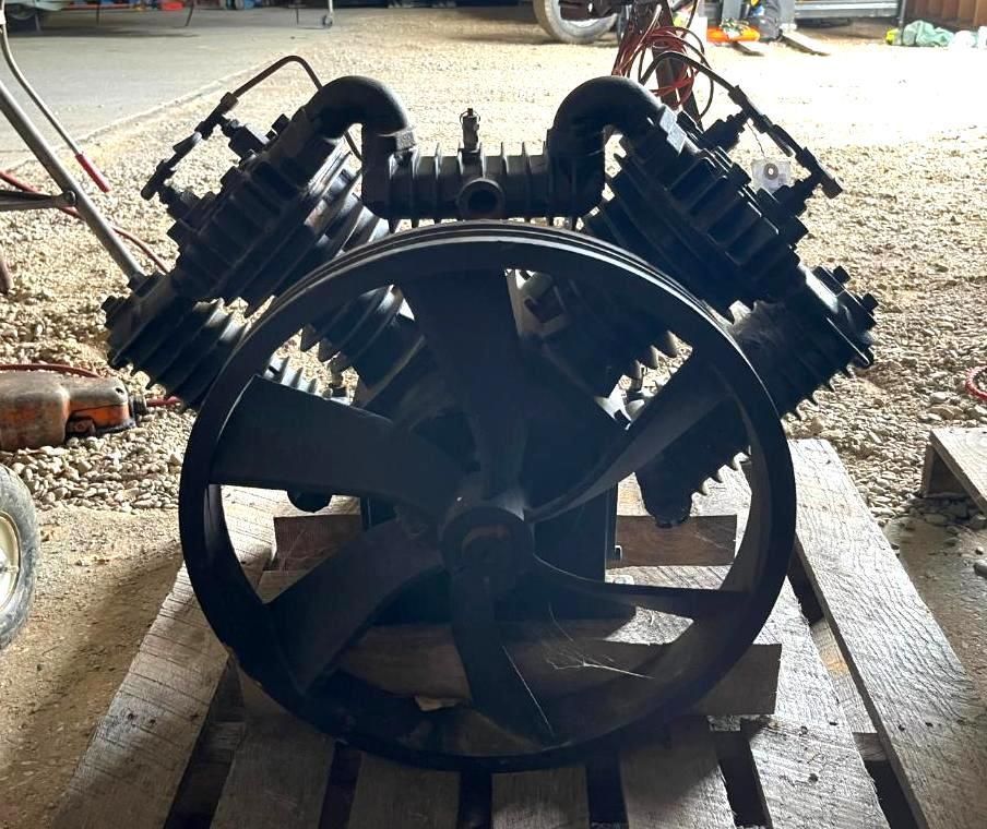 Black industrial air compressor with a large fan and pulley on a wooden pallet.