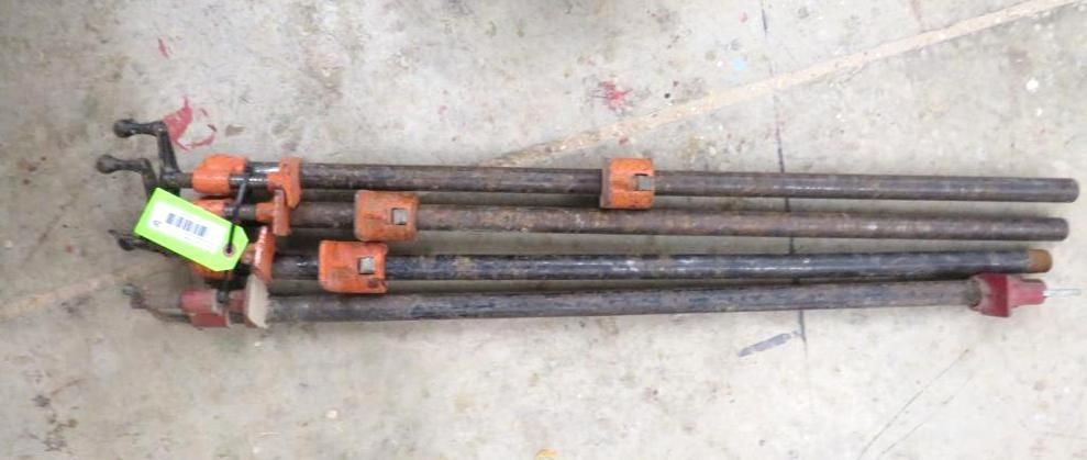Six metal poles with orange and red adjustment pieces lie on a concrete surface.