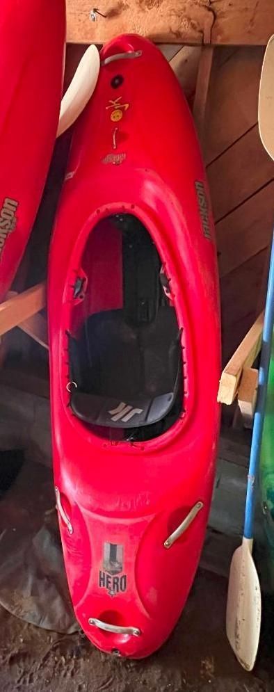 Red kayak with a large cockpit, stored inside a wooden structure.