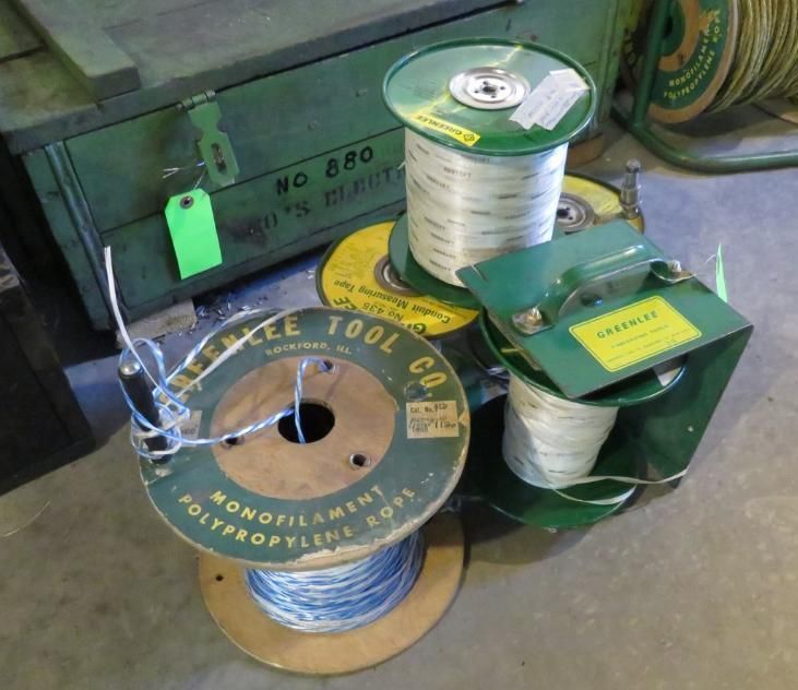 Spools of rope and wire, some labeled, next to a green wooden box and a spool holder.