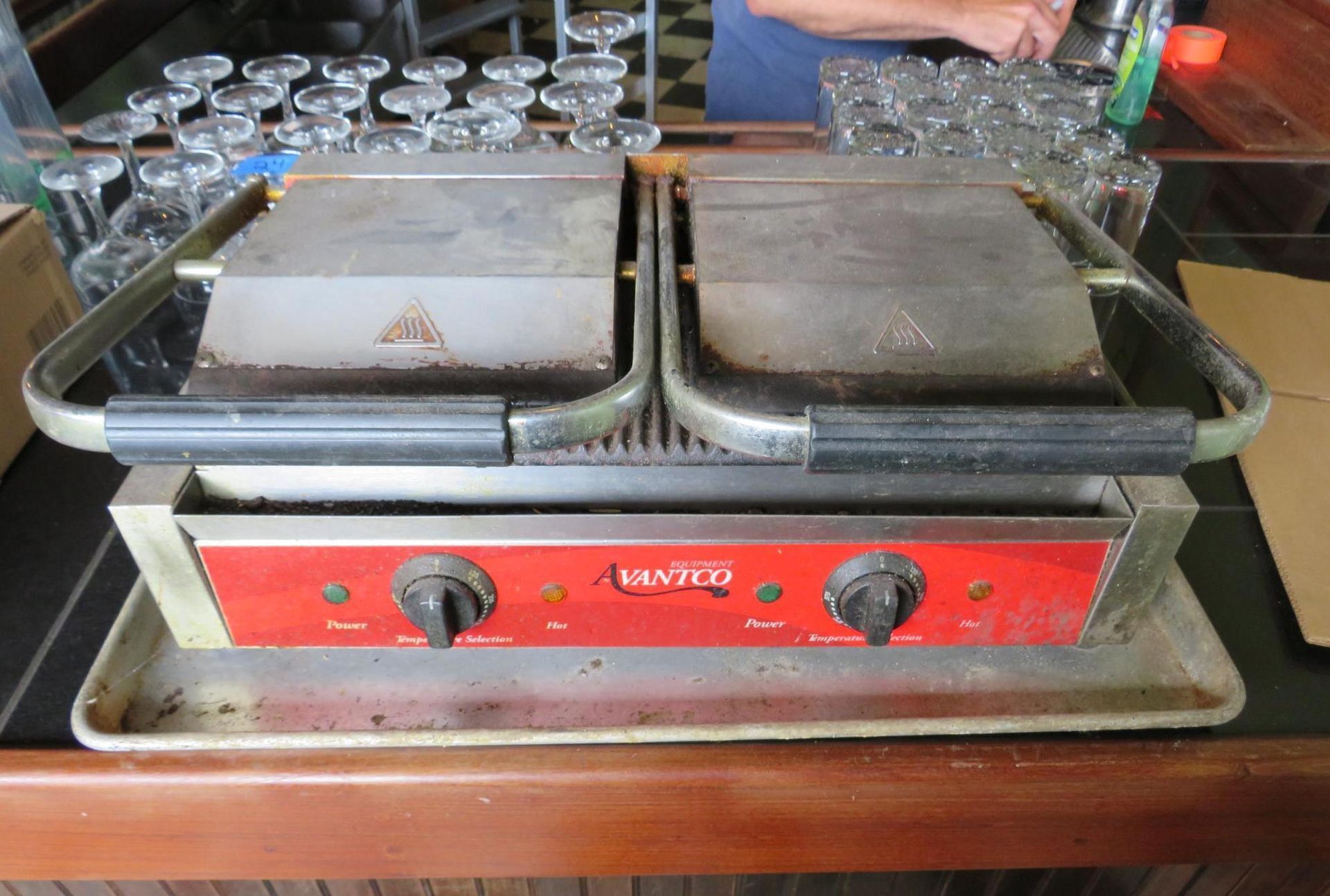A commercial panini press with two heating surfaces, red front panel.