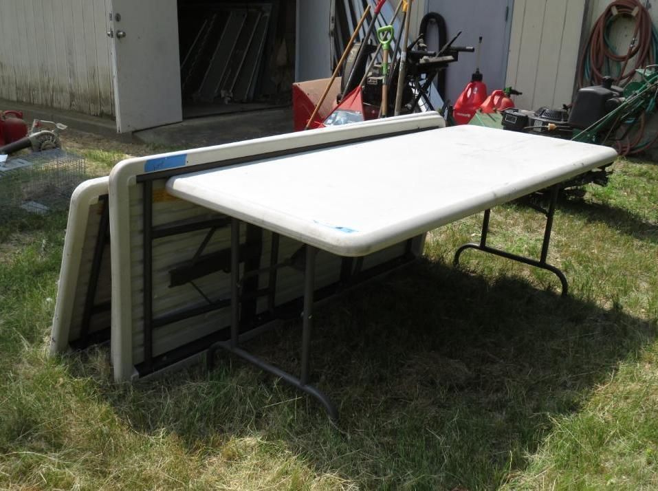 Two folding tables are set up outdoors on grass. One is upright, the other folded.