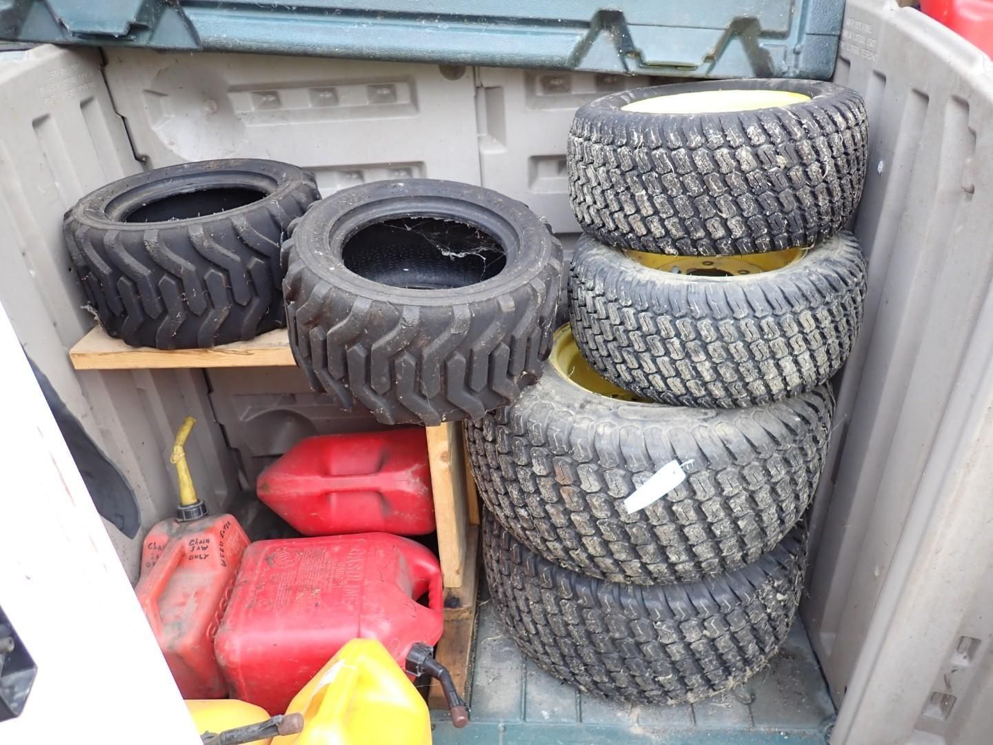 Stacked off-road tires and red gas cans in a metal storage container.