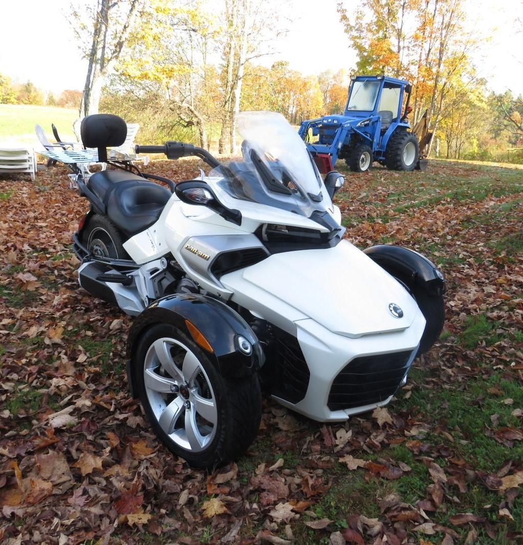 White Can-Am Spyder motorcycle with three wheels on a leaf-covered lawn.