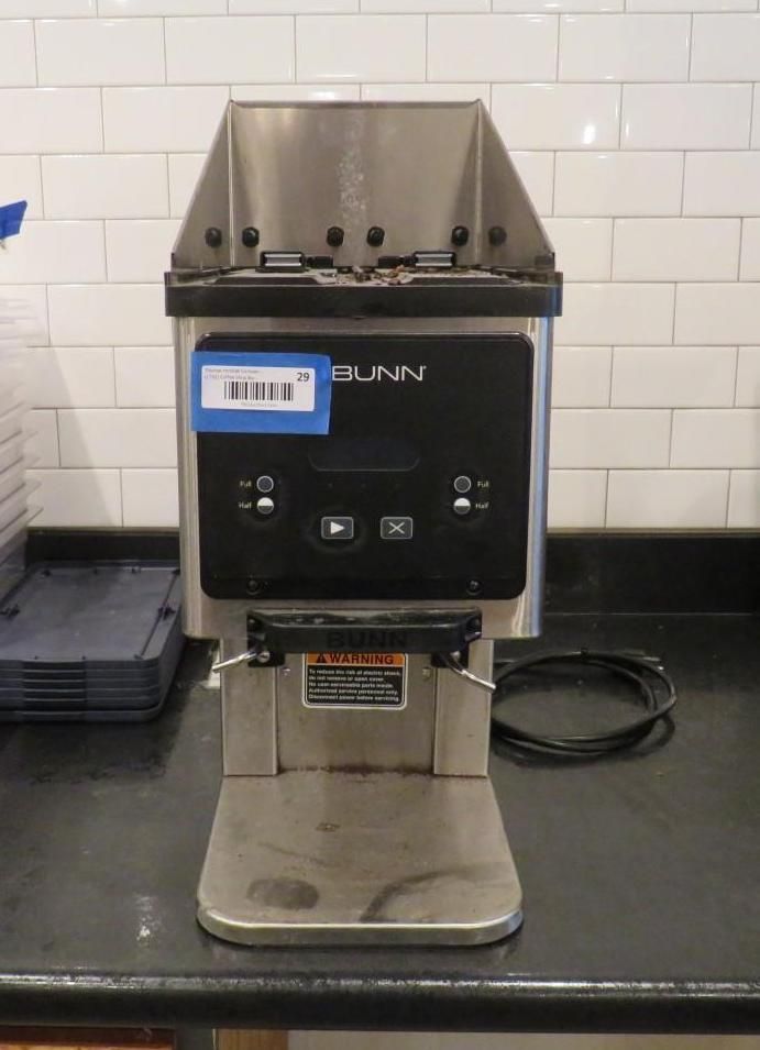 Stainless steel BUNN coffee machine on a black countertop, in front of a white tiled wall.