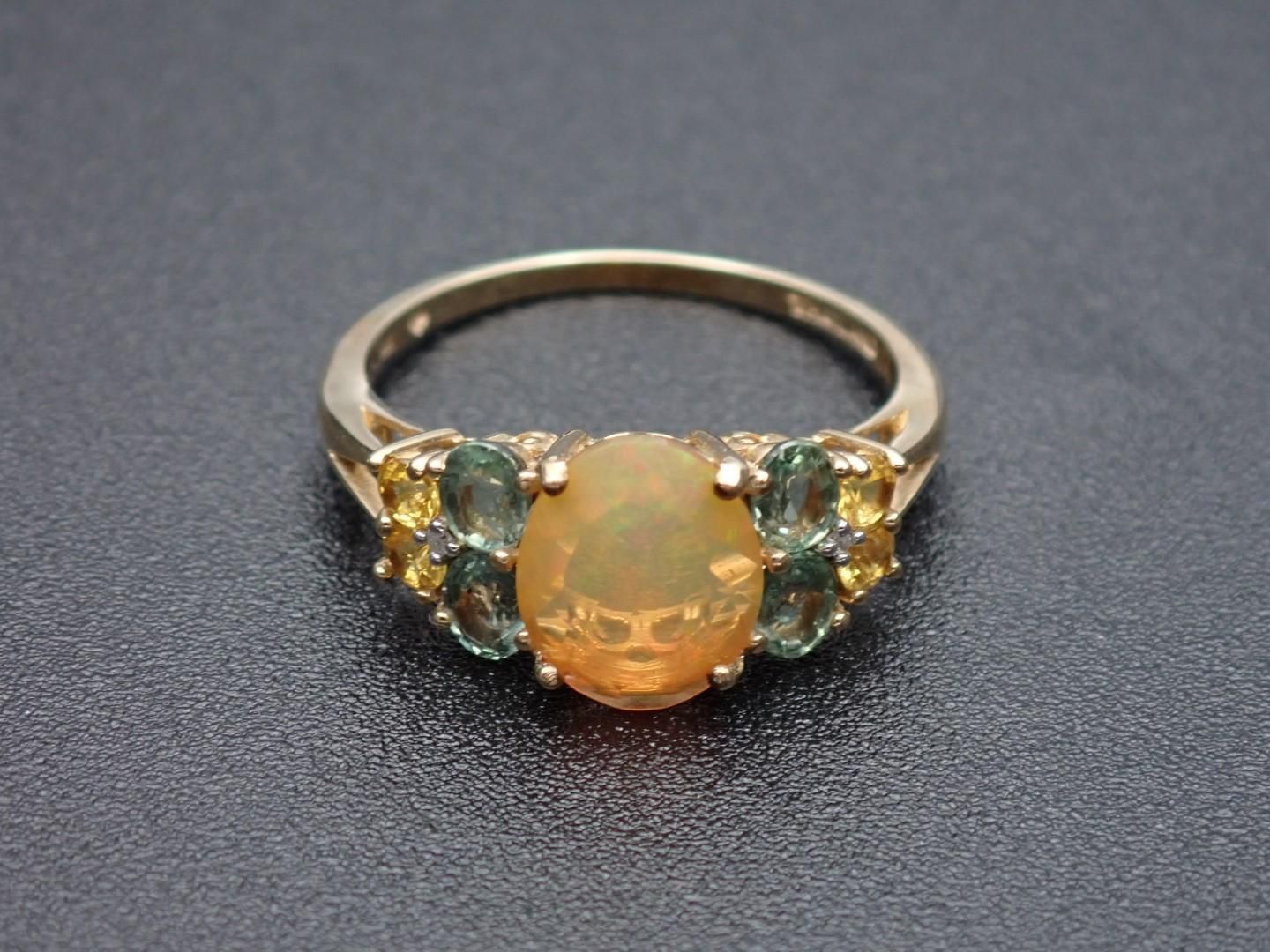 Gold ring with an oval orange center stone and smaller green and yellow side stones.