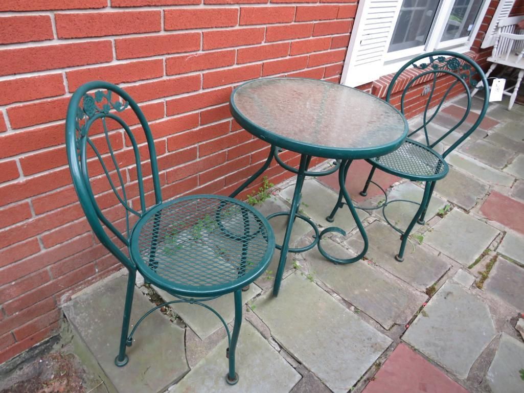 Green metal patio table and chairs on a stone patio next to a brick wall.