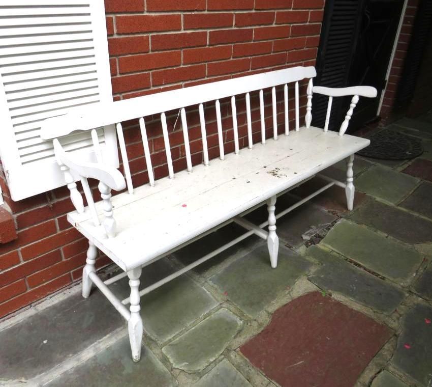 White wooden bench with a back and armrests on a brick patio.