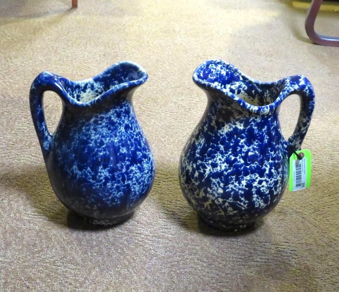 Two blue and white speckled pottery pitchers on a beige surface, each with a handle and ruffled rim.