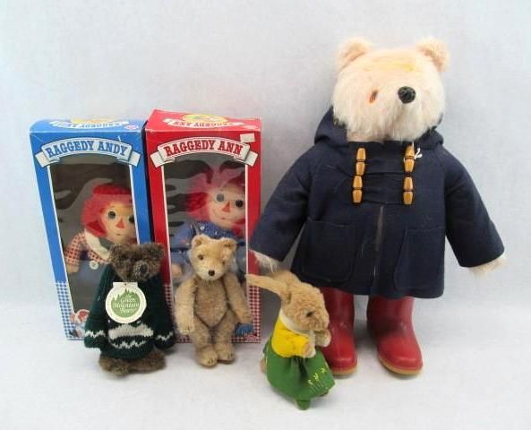 Teddy bears and Raggedy Ann dolls, in boxes, a bunny, and a bear in a coat and boots.