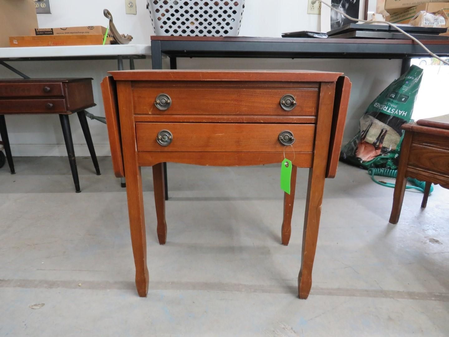 Wooden drop-leaf side table with two drawers. Cherry finish, ornate drawer pulls, and slender legs.