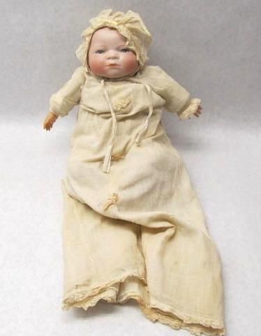 Antique bisque baby doll in cream-colored gown and bonnet, arms outstretched.