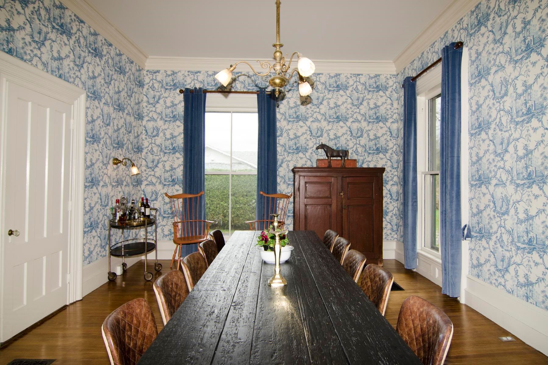 Formal dining room with blue patterned wallpaper, long dark wood table, and wooden chairs.
