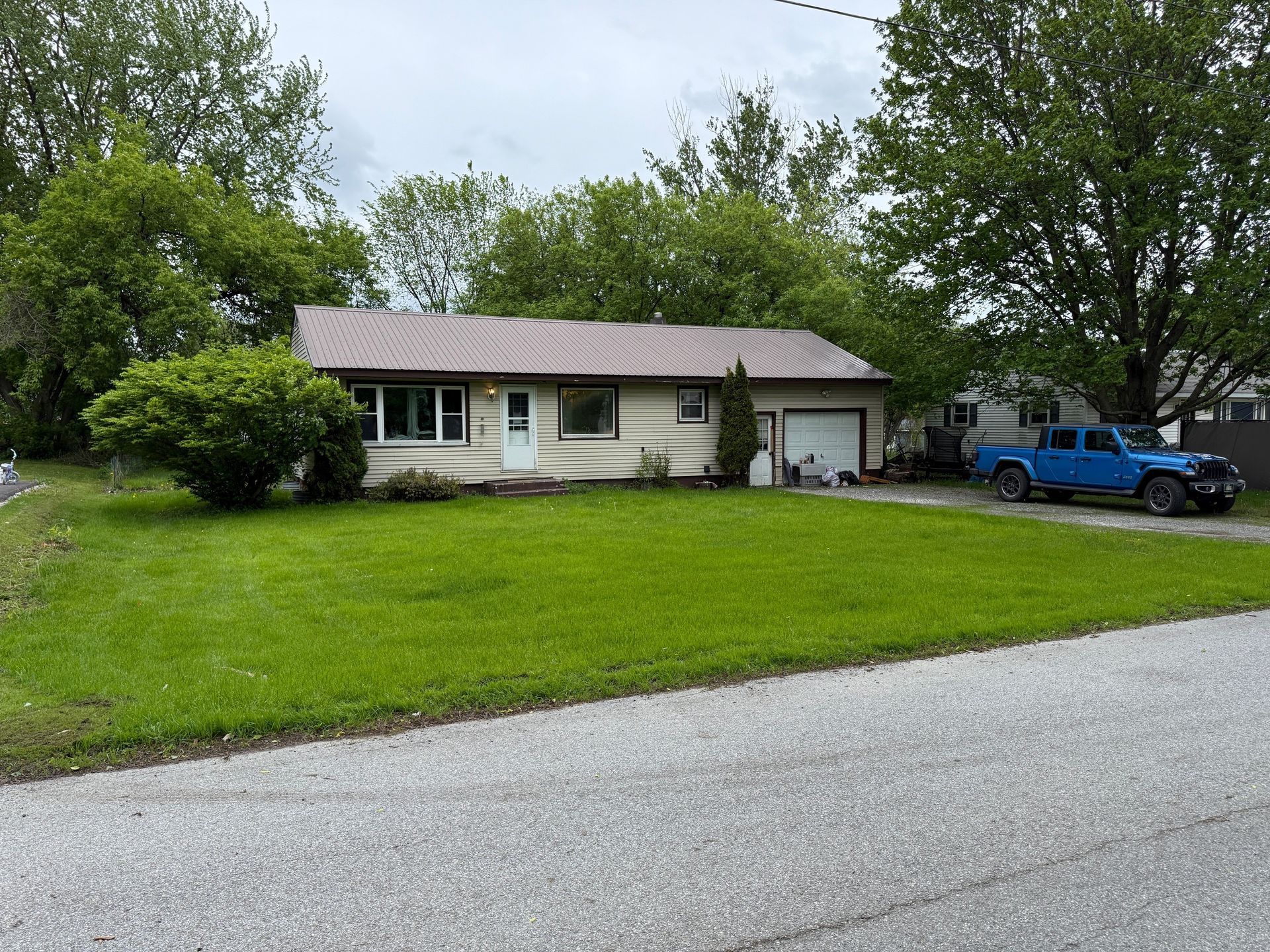 Single-story beige house with a metal roof and attached garage. A blue truck is parked in the driveway.