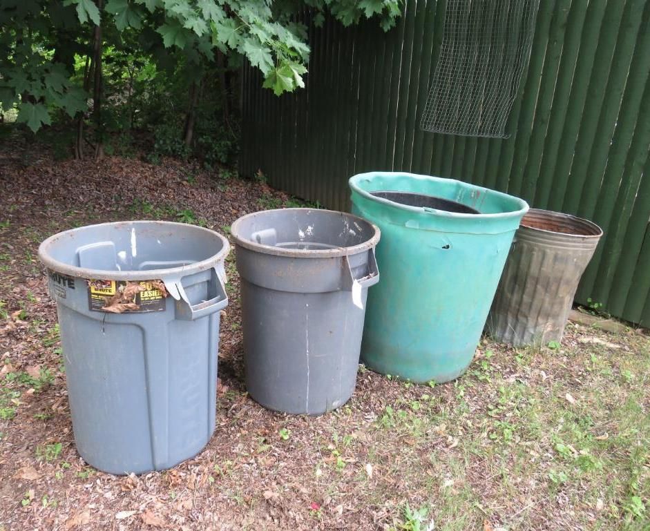 Four trash cans of varying sizes and colors sit outdoors near a green wall and foliage.