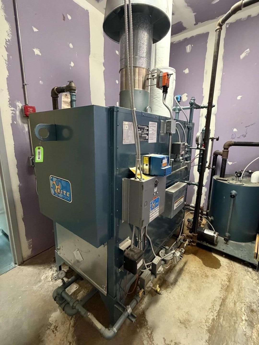 A large, blue boiler with various pipes and gauges in a utility room.